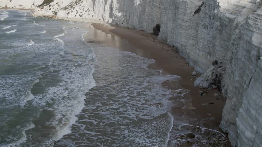 Waves roll ashore at the base of a rock formation