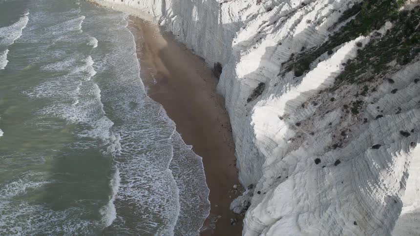 Waves wash ashore below a steep cliff