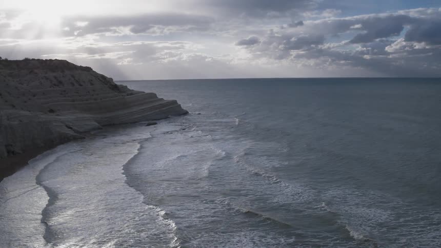 Waves roll towards the coastline under a cloudy sky