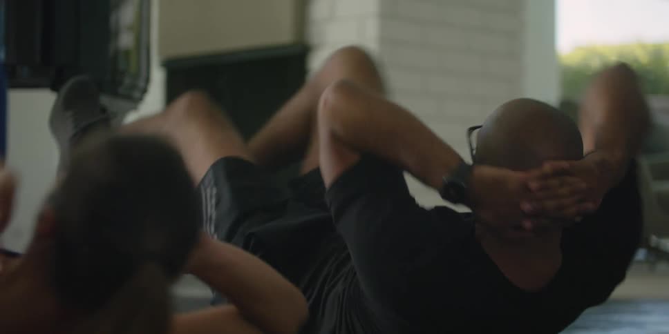 A man does crunches alongside a woman on an exercise mat indoors during the day