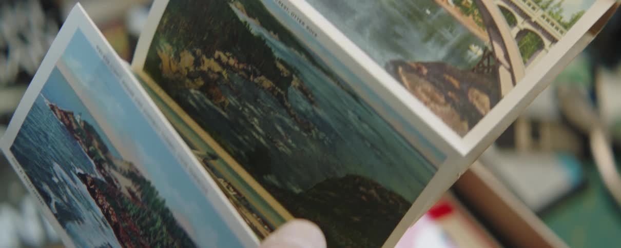 Closeup of mans hands holding postcard of bridge beach coast and coastal town