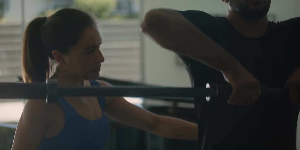 A man lifts a barbell while being instructed by a personal trainer