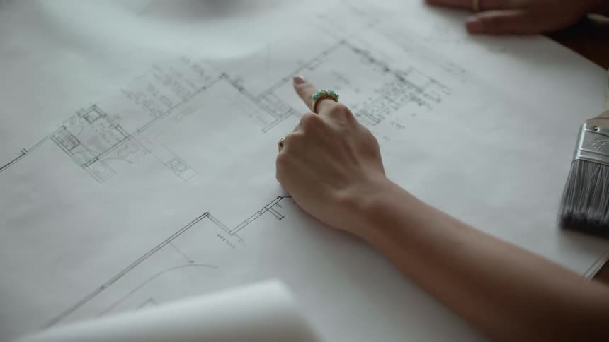 Close up of the hand of a woman pointing at a paper floor plan on a table