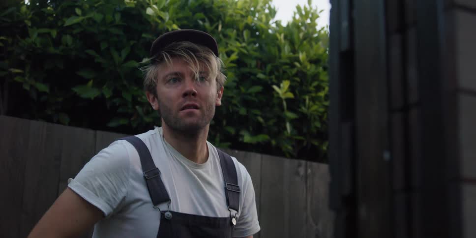 Man crouching on the backyards wearing overalls stands up to look at something at morning