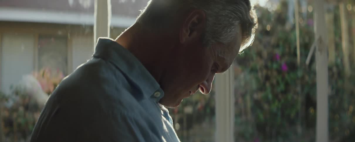 Sun shines behind a mature man standing in a room at home in the morning