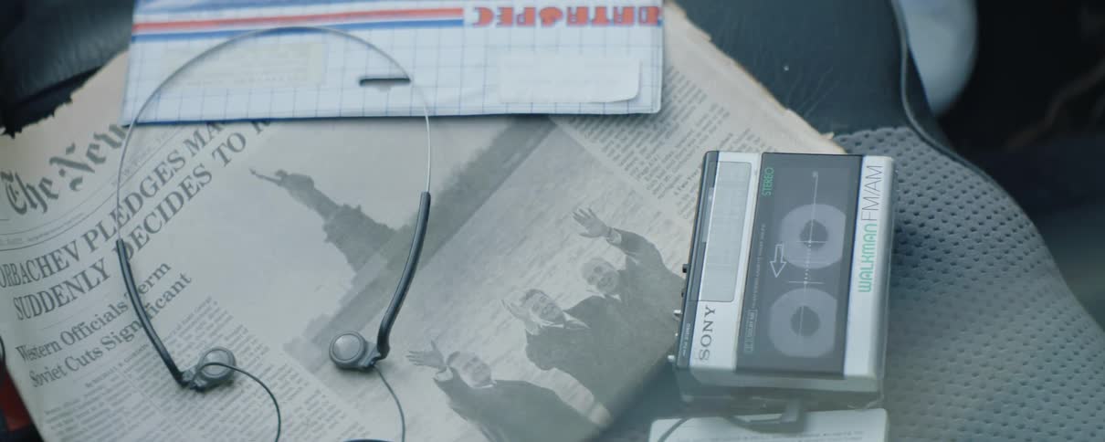 Earphones are lying on top of a newspaper with the statue of liberty next to a cassette tape player