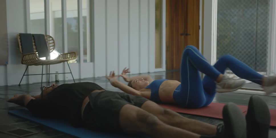 Female exercise instructor guides man through floor exercises