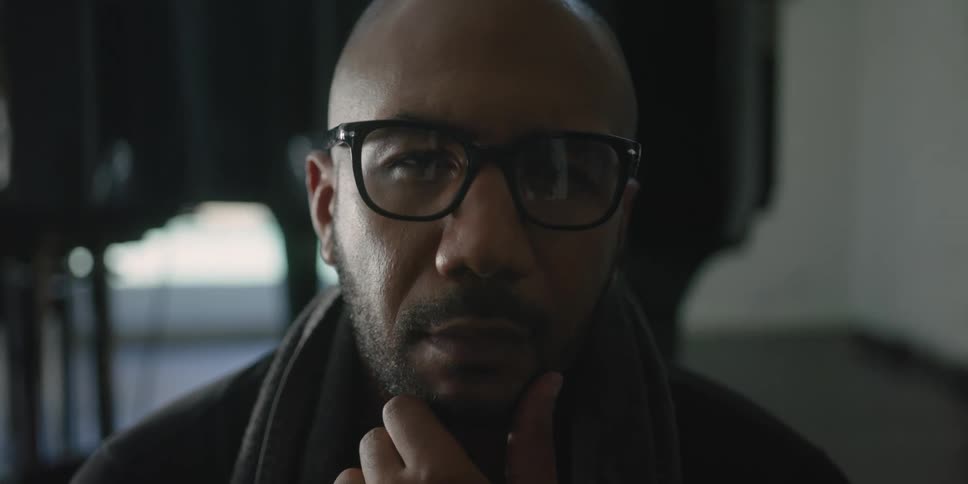Man wearing glasses strokes beard while thinking
