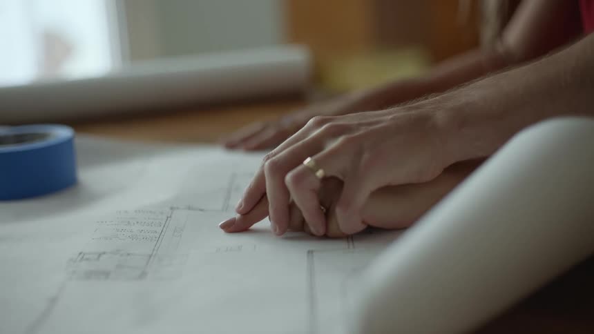 A person guiding another persons hand over a floor plan spread out on a table