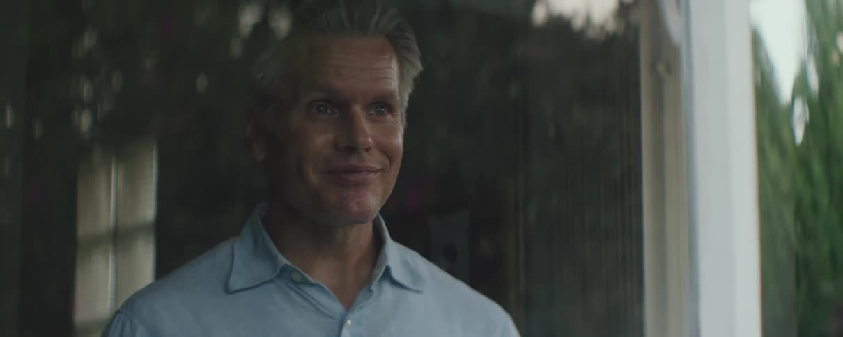 A man smiles while looking through a window at home