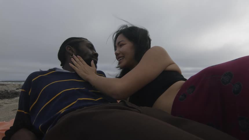Couple cuddles while lying down on beach on windy overcast day