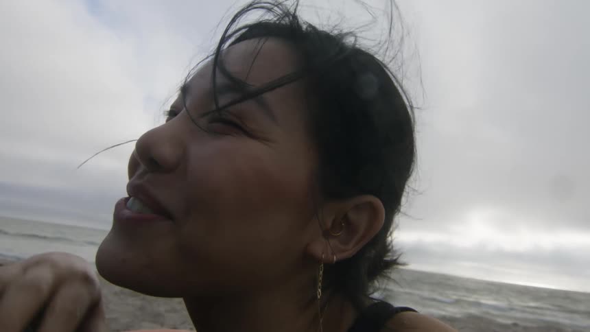 Woman lies on sandy beach smiling and talking on an overcast day