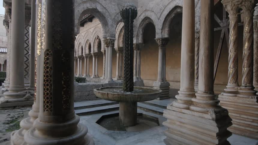 A water fountain inside some architecture with pillars and surrounding by buildings with arches
