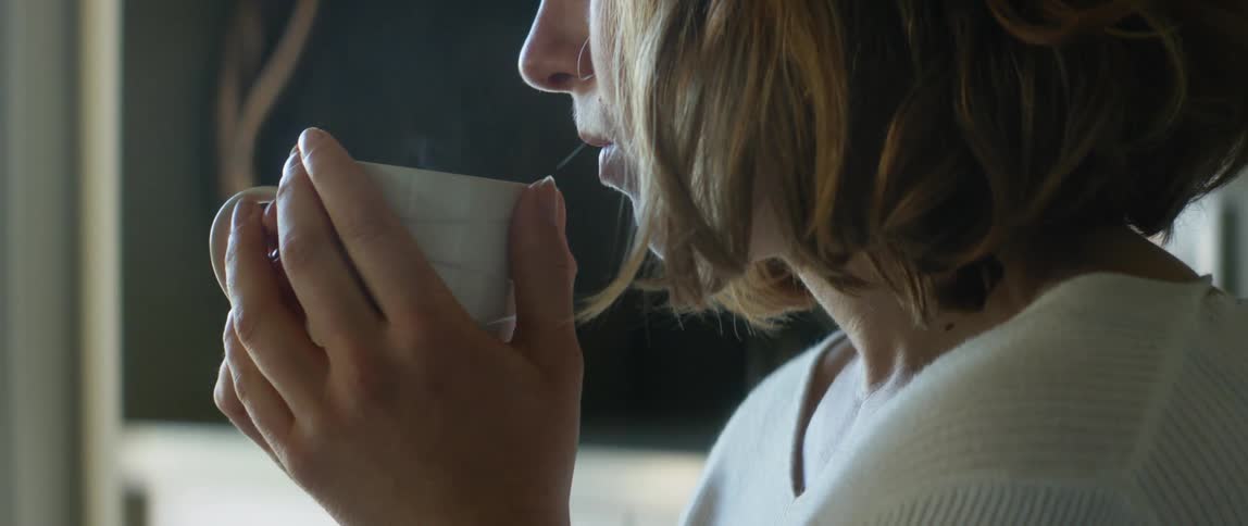 A woman is drinking a cup of coffee indoors