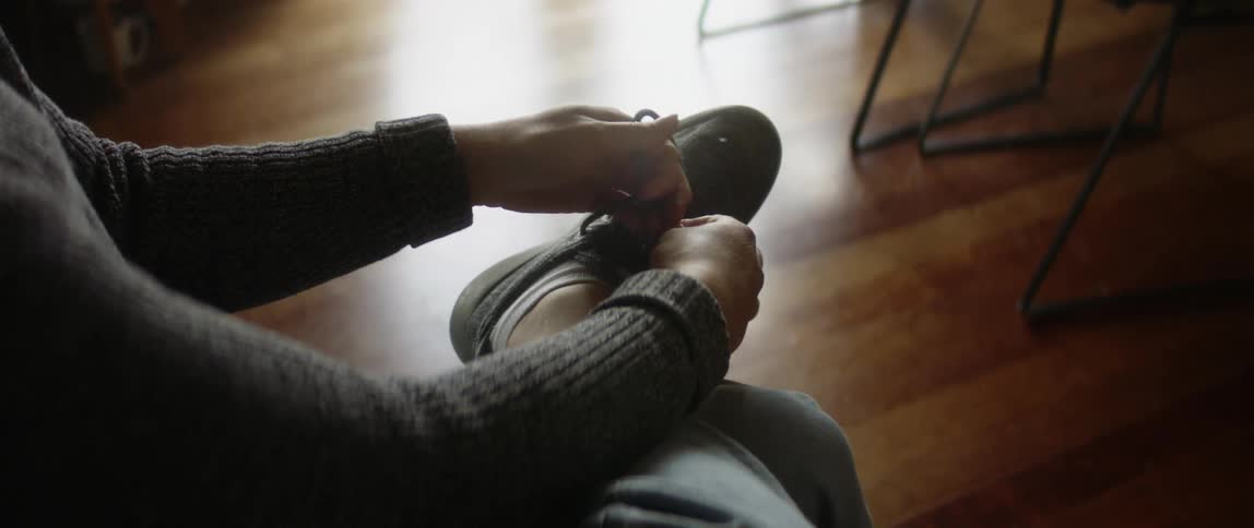 A woman at home puts her shoes on as her dog walks past her