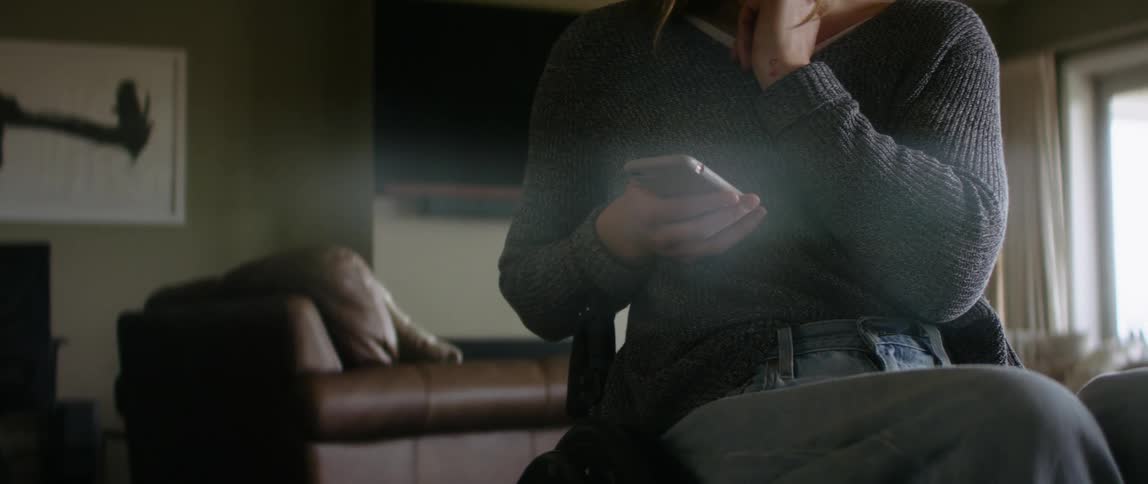 Young woman sitting on a wheelchair in the living room looking at her phone