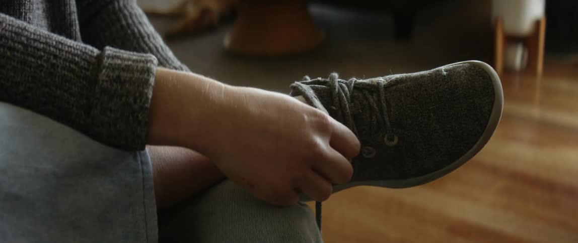 A girl puts her foot with a sock on her knee and puts on her shoe and ties it then puts her foot on the floor