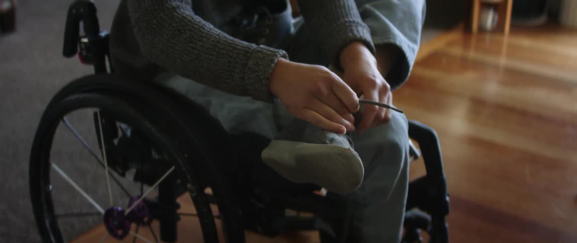Young woman sitting on a wheelchair ties the laces on her shoes in the living room