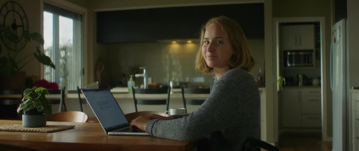 Young woman sitting on a wheelchair working on a laptop at home looking at the camera
