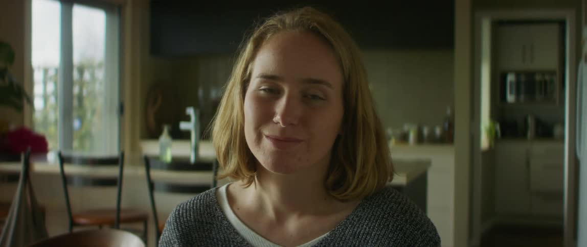 Blonde female wheelchair user smiles at camera in the kitchen