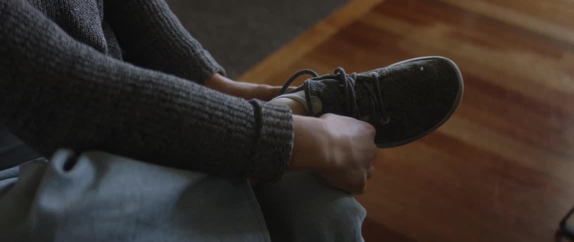 Blonde female wheelchair user wearing gray sweater white socks and jeans wears shoes