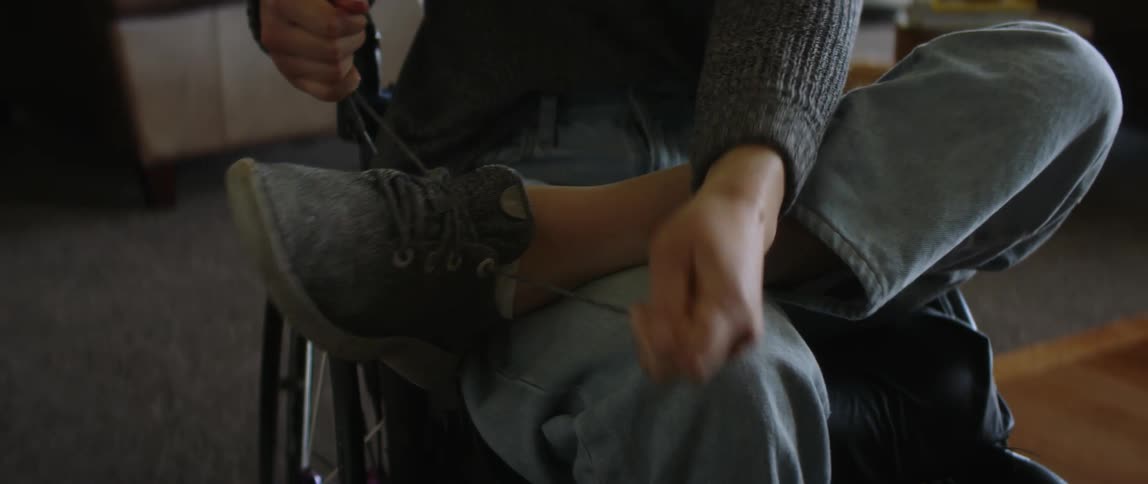 A woman in a wheel chair sits at home and puts her shoes on