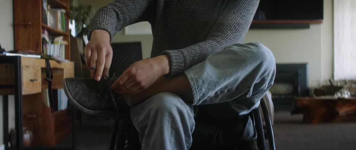 Blonde female wheelchair user wearing gray sweater white socks and jeans wears shoes
