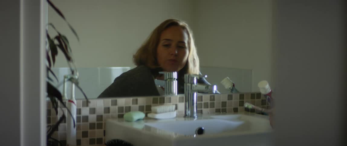 A woman is in a bathroom and brushing her teeth