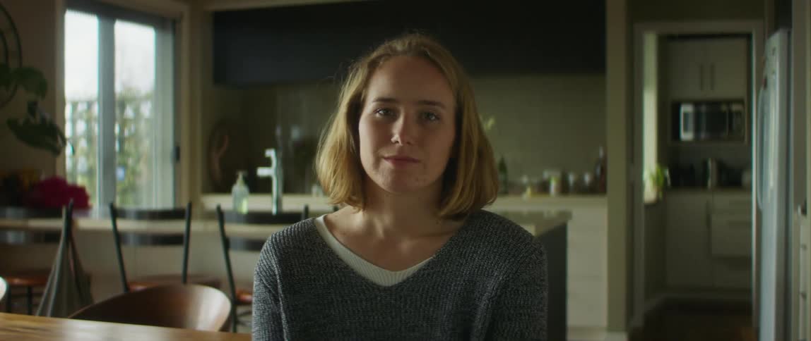 A woman looks into the camera while sitting inside a house during the day