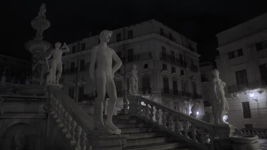 Stone statues stand on staircase railing between buildings