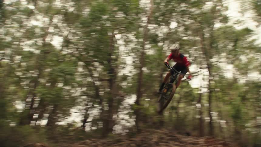 Cyclist rides bike along trail through woods making a jump