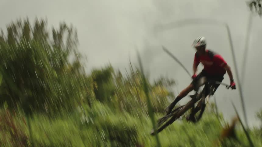 A cyclists does a trick in the air after going airborne while riding along a dirt trail through the countryside on a cloudy day