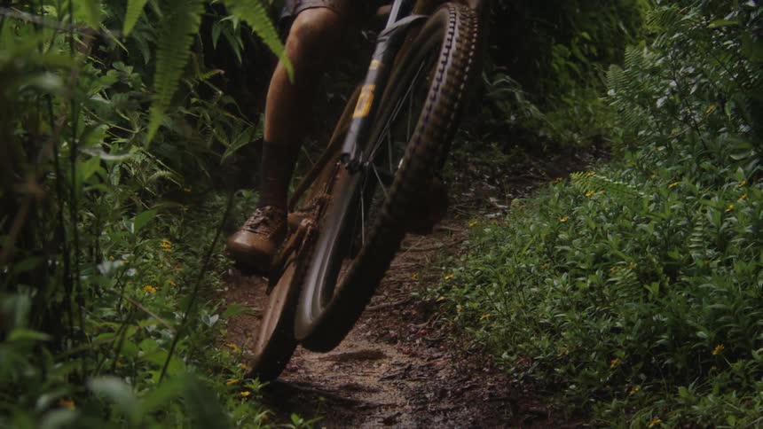 A mans legs are coated in mud while he rides through a dirt trail in the woods