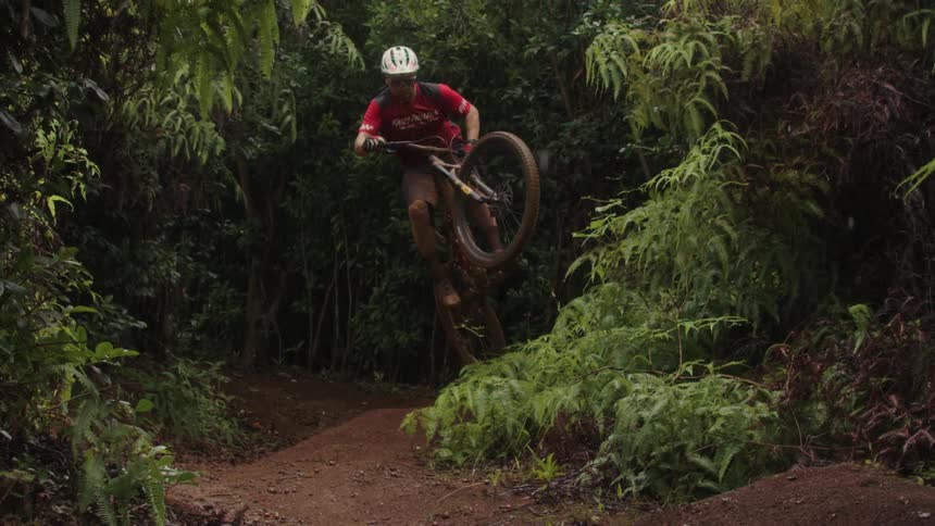 A man is shown jumping in the air on his bike on a dirt road in the woods in slow motion