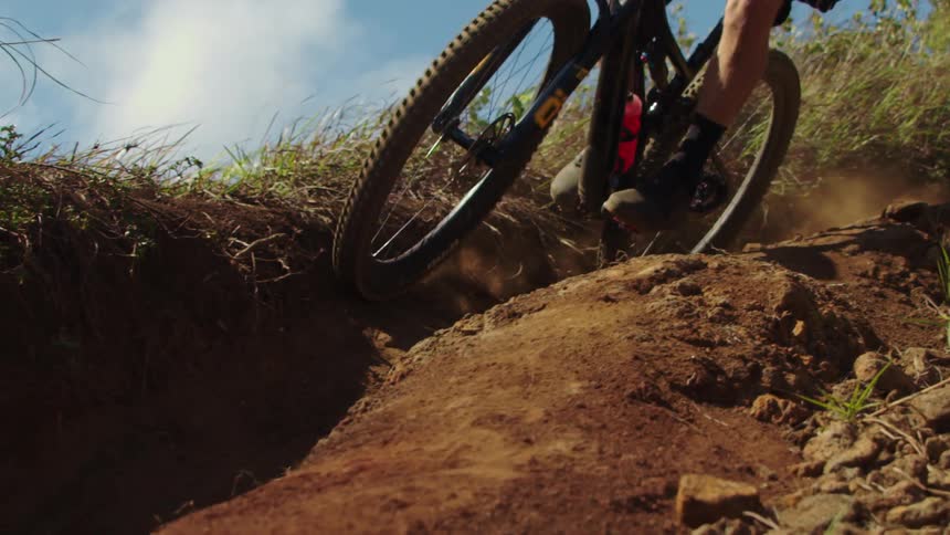 Cyclist rides bike along uneven sloping dirt path moving down hill