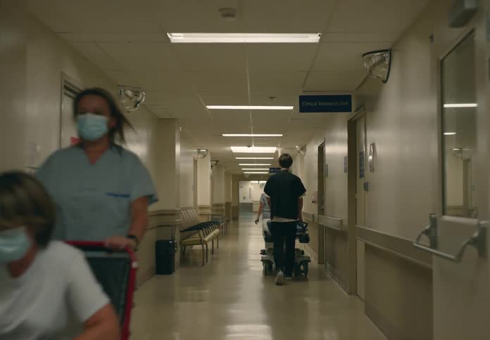Patients in a wheelchair and a bed are being pushed down a hospital hallway