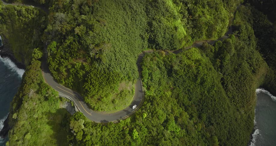 Vehicles travel along a winding mountain road overlooking the ocean during the day
