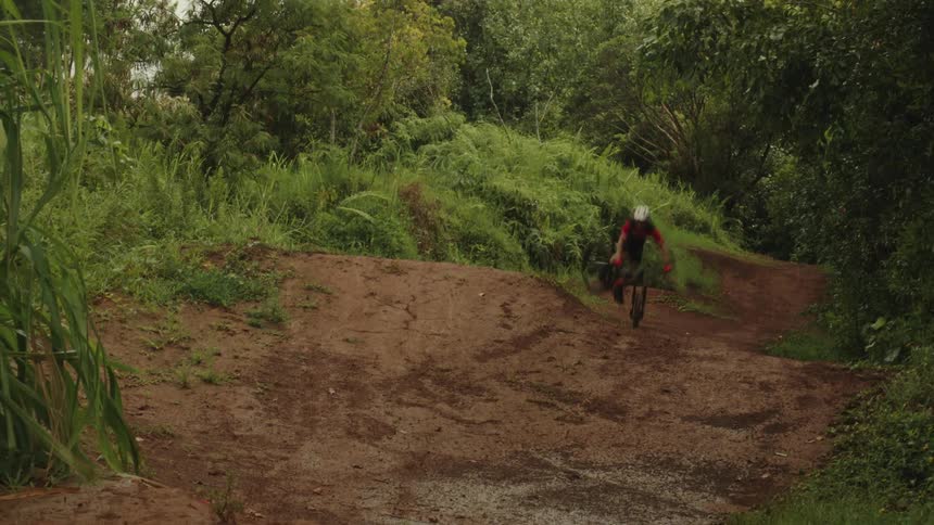 Biker rides mountain bike over several dirt ramps in the woods