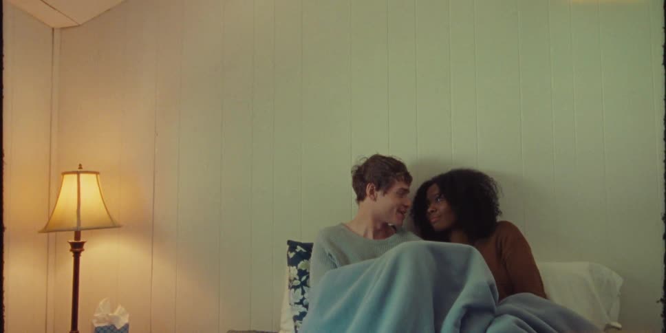 Young couple in love cuddling while sitting on bed looking at each other and laughing