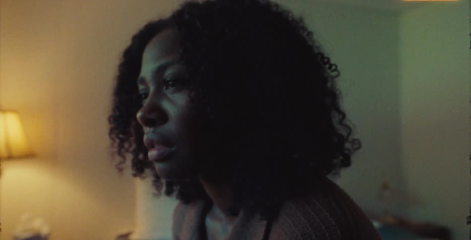 Black woman sitting in her bedroom with a thoughtful and sad expression on face