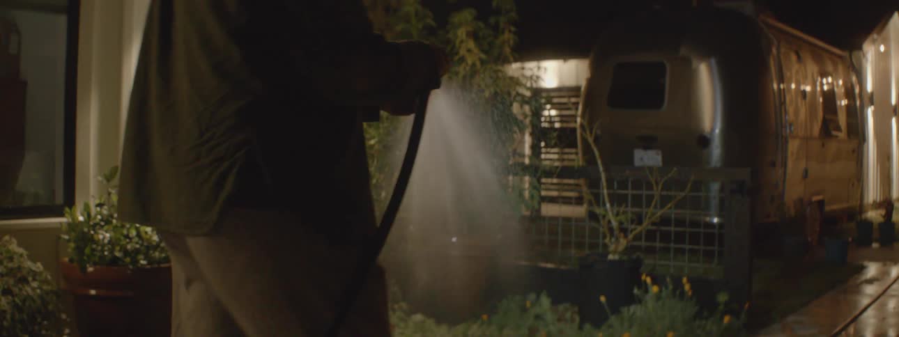 Older man waters plants at night using a water hose