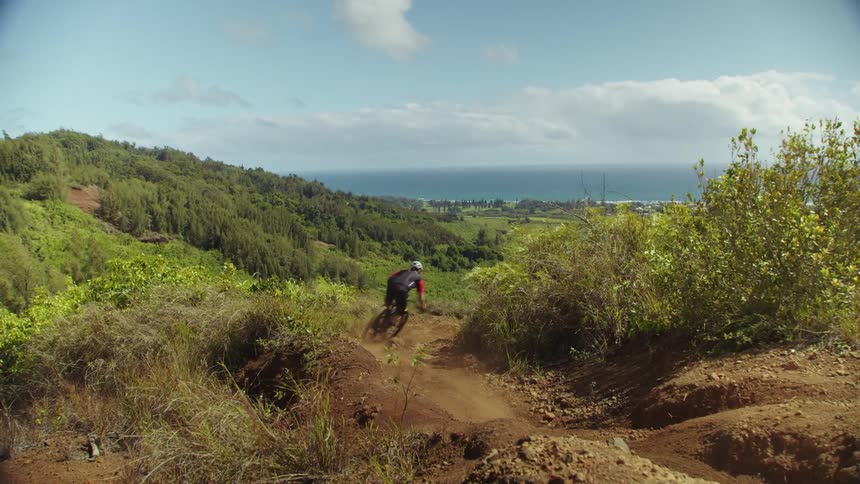A cyclist rides a bicycle offroad over rugged terrain in a hilly countryside during the day