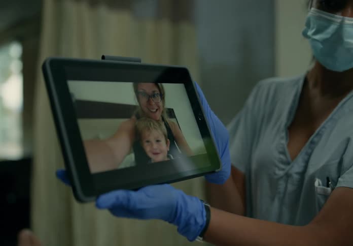 A nurse holds up a tablet so a patient can speak to family