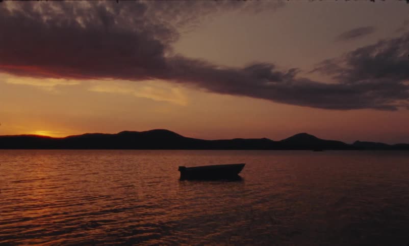 Empty canoe in the middle of a lake during sunset with hills in the background