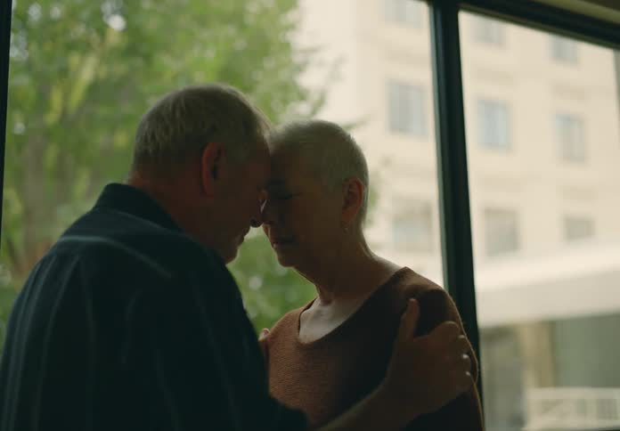 Man comforts upset woman while they stand near window showing building