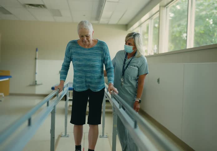 An elderly woman walks during therapy as a therapist encourages her