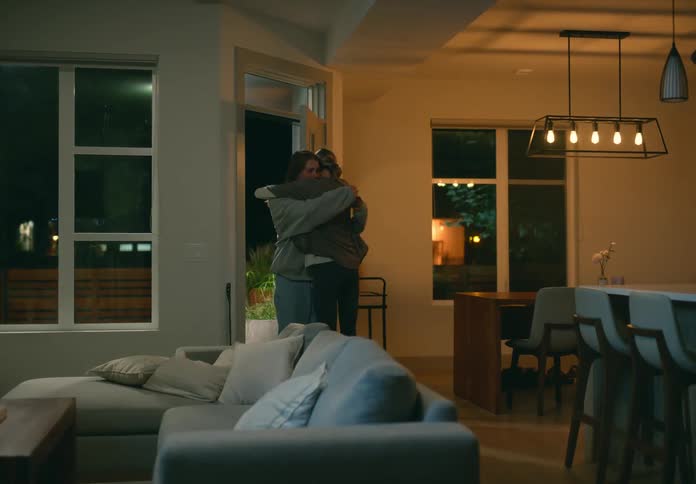 Woman sitting on a couch at home stands up in a hurry to hug a woman entering the door