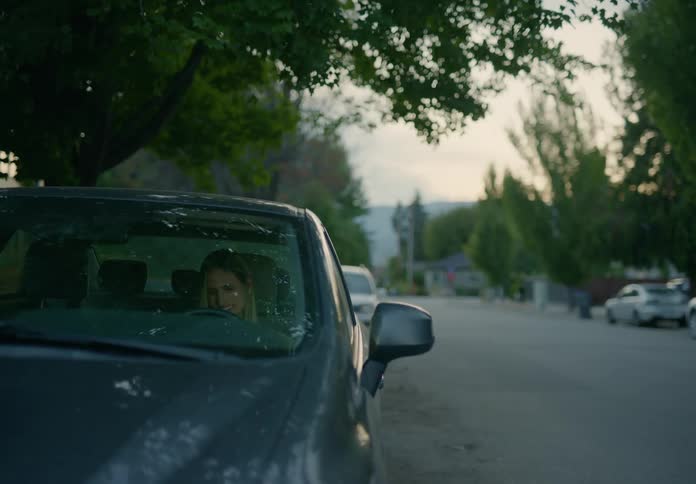 A woman yells and cries while sitting in a car parked on the roadside in a residential neighborhood during the day