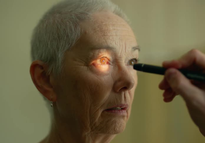 A medical professional examines the eyes of an elderly patient using a small flashlight