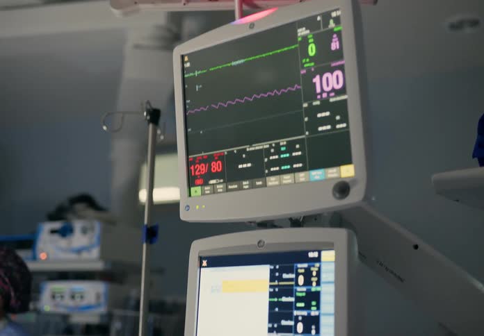 A medical worker adjusts a vital sign monitor in an operating room
